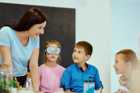 Teacher guiding curious children during a hands-on classroom science experiment with safety goggles and test tubesの写真素材