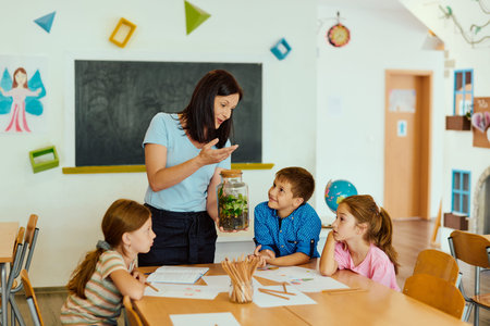 Teacher showing a terrarium to engaged elementary students during a hands-on science lesson in classroomの写真素材