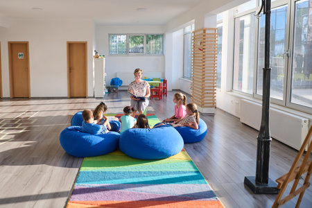 Teacher reading aloud to children sitting on blue beanbags during a bright classroom story time sessionの写真素材