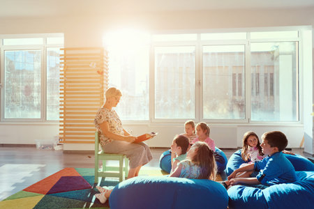Teacher reading a story to young children during group storytime in a bright classroomの写真素材