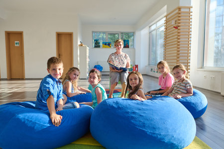 Children listening to teacher reading on blue beanbags in a bright classroom circle sessionの写真素材