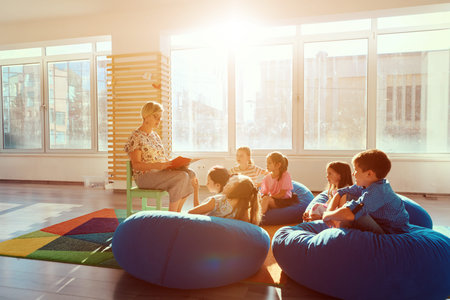 Teacher reading story to children during classroom storytime on beanbags in a bright preschoolの写真素材