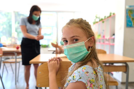 Young student wearing a face mask in a classroom with teacher enforcing safety during pandemicの写真素材