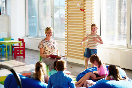 Teacher reading to children during storytime in bright preschool classroom with kids laughing and learningの写真素材