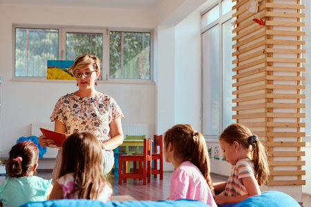 Preschool teacher reading a story to attentive children during circle time in a bright classroomの写真素材