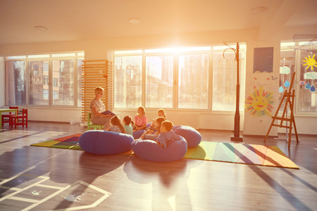 Teacher reading to children on bean bags during storytime in a bright preschool classroomの写真素材