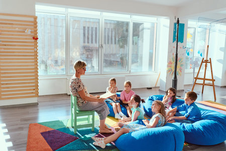 Teacher reading a story to young children gathered on beanbags in a bright classroomの写真素材