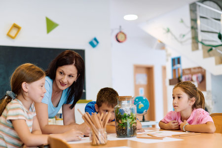 Teacher guiding children around a classroom terrarium during a hands-on science activityの写真素材