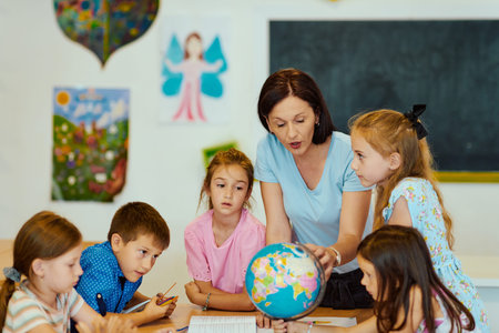Teacher showing globe to attentive elementary students during group geography lesson in colorful classroomの写真素材