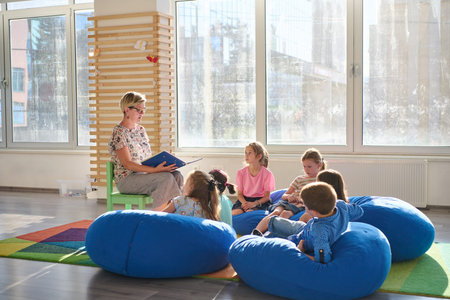 Teacher reading a picture book to young children during cozy classroom circle time on bean bagsの写真素材