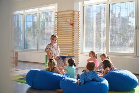 Female teacher reading to young children during storytime in a bright classroom seating areaの写真素材