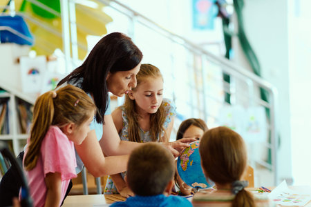 Teacher and children examining a globe together in a bright classroom during a geography lessonの写真素材