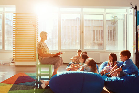 Teacher reading a story to children during storytime in a bright sunny classroomの写真素材