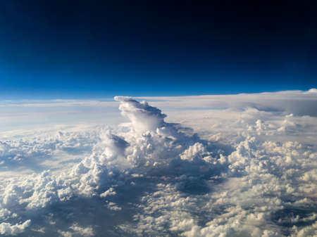 Aerial view of uniquely shaped white cumulonimbus clouds below on dark blue backgroundの写真素材