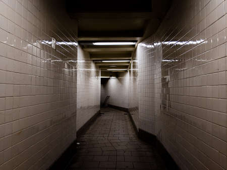 Dark hallway with reflective white tiles and bright lights to subway trains in New York Cityのeditorial素材