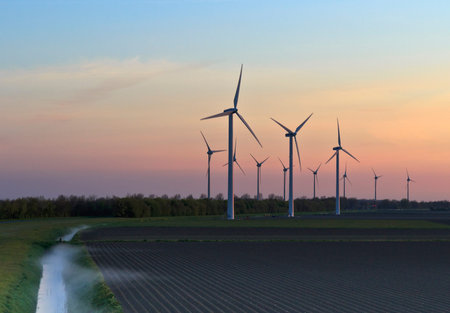 Wind turbines during sunrise in a plowed field.