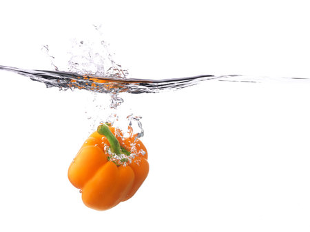 Orange bell pepper falling into water, with a splash, white background の写真素材