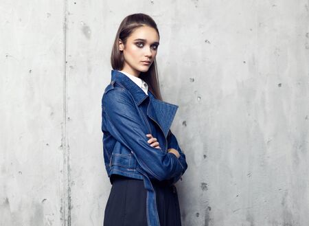 Fashion model wearing denim jacket and long black skirt posing in studio on concrete wallの写真素材