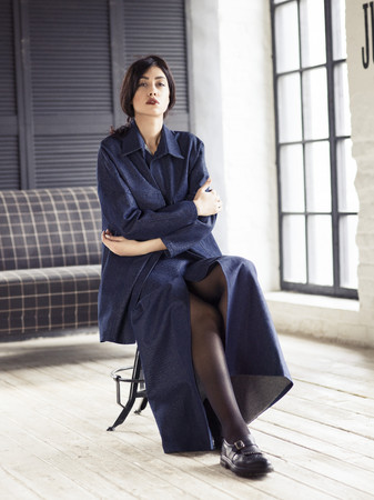Elegant woman wearing denim suit sitting in studioの写真素材