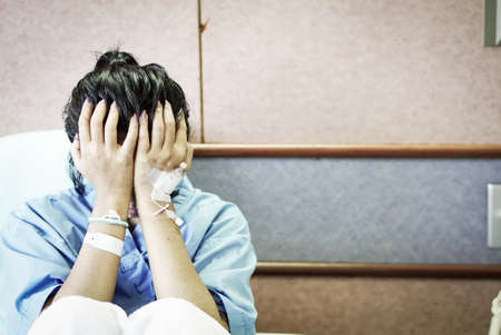 A depressed Asian female patient covering her face with her two hands while lying in a hospital bed waiting for her treatment, concepts of healthcare, attitude to life and depression.の写真素材