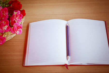 top view of office desk with an open notebook,a pencil and bunch of pink flowers on a wooden table with copy space for text.の写真素材
