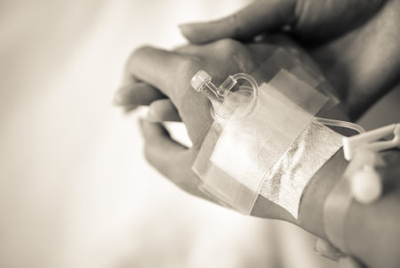 closeup of a nurse carefully holding a patient's hands with intravenous catheter in a hospital;...