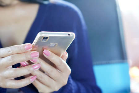close up of a woman's hand holding her smart phone while sitting on an office chairの写真素材