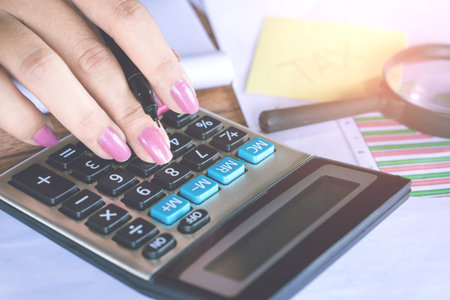 woman hand calculating  her monthly expenses during tax season. hand counting on calculator with...