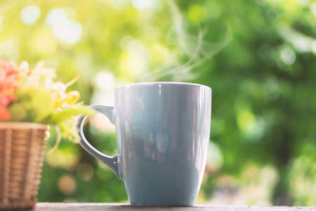 hot coffee mug on wooden table over nature green background with morning sunlightの写真素材