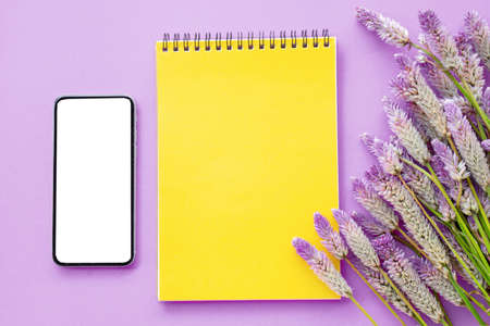 top view blank yellow paper with purple flower and smart phone flat lay composition on purple background ,template for textの写真素材