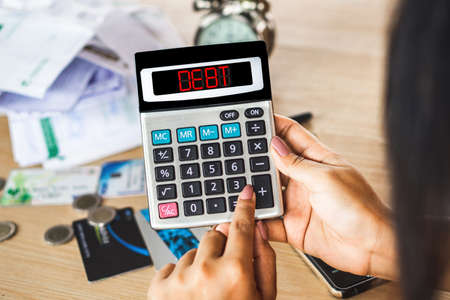 woman hand calculating her expenses with unpaid financial bills ,credit cards on desk with word debt on calculatorの写真素材