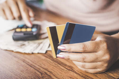 woman hand calculating  her expenses and debt from credit cards with money on deskの写真素材