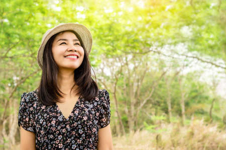 beautiful asian woman wearing a hat and smiling outdoors in green parkの写真素材