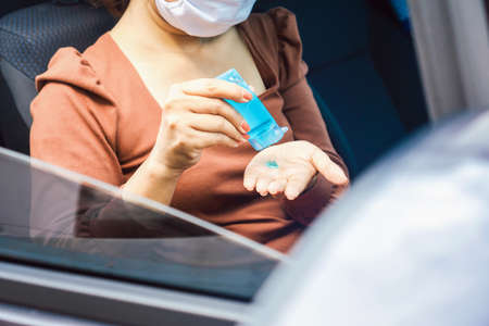Asian woman sitting in a car applying hand sanitizer alcohol gel to clean her hand and wearing protective mask before driving during covid-19 pandemic, new normal lifestyle concept backgroundの写真素材