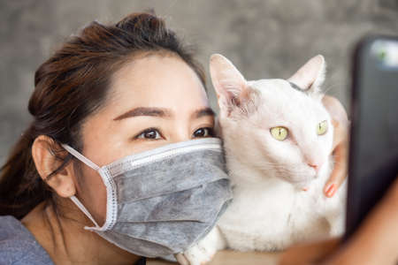 Asian woman wearing medical mask and playing and hug her cat during covid-19 outbreak, social distancing and new normal lifestyle conceptの写真素材