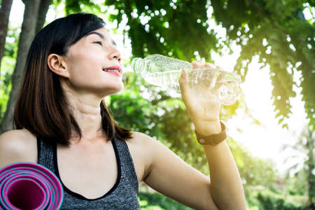 sport Asian woman drinking water from bottle another hand holding yoga matの写真素材