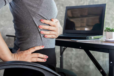 woman suffering from office syndrome having lower back pain sitting on chairの写真素材