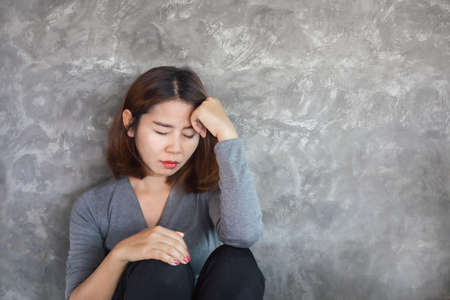 sad Asian woman sitting alone against the wall feeling depressed and lonelyの写真素材