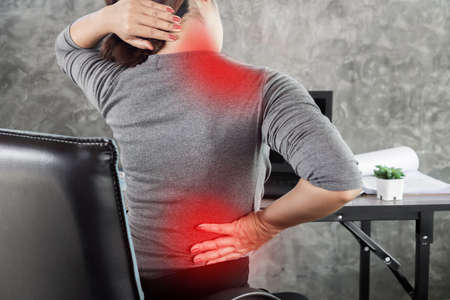 woman suffering from office syndrome having lower back pain, neck and shoulder pain sitting on chairの写真素材