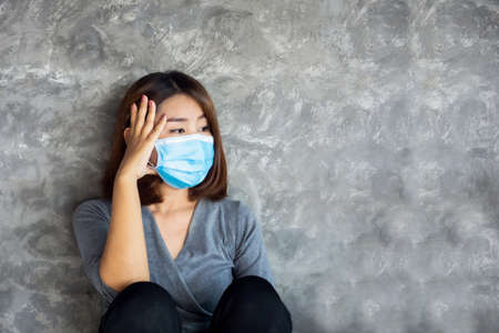 depressed Asian woman wearing  face mask sitting alone next to the wallの写真素材