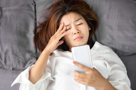 Asian woman rubbing her eyes tired from watching series from smart phone  late at nightの写真素材