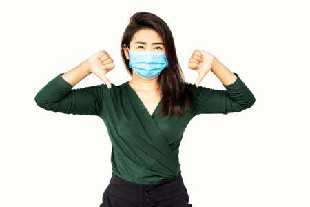 unhappy business Asian woman wearing protective mask with hand sign dislike, thumbs down ,negative emotionの写真素材