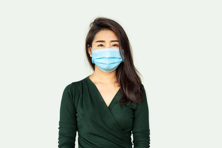 unhappy Asian woman wearing protective mask with sad face standing over grey background