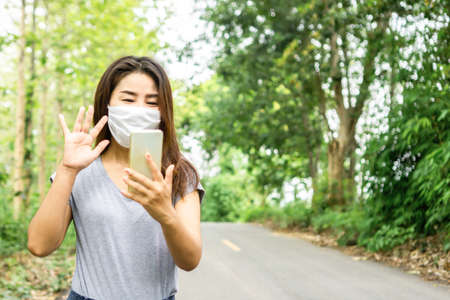 Asian woman wearing protective mask and using smart phone to video call with someone ,new normal and social distancing during covid-19 pandemicの写真素材