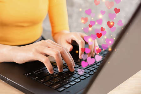 online dating concept with woman hand chatting on computer hand typing on keyboard with heart shape flyingの写真素材