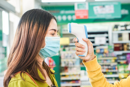 worker hand holding temperature scanner checking fever of customer that wearing protective mask...