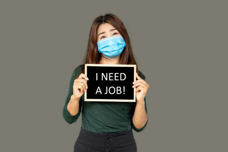Asian business woman wearing protective mask hand holding a sign need a job ,Coronavirus or COVID-19 crisis conceptの写真素材