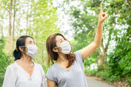Asian mother and daughter wearing protective mask and walking together in a park enjoy travelling in nature , new normal lifestyle conceptの写真素材