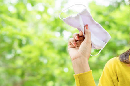 woman hand throwing face mask away over nature background out door, back to normal life, after coronavirus and quarantine is over conceptの写真素材