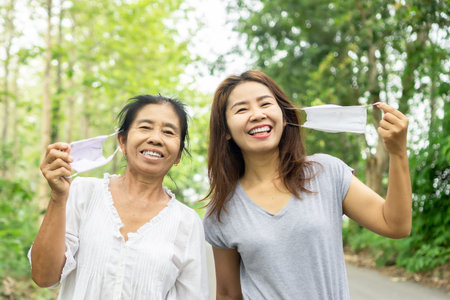 happy Asian mother and daughter traveling outdoors hand take off face mask and laughing ,happy...